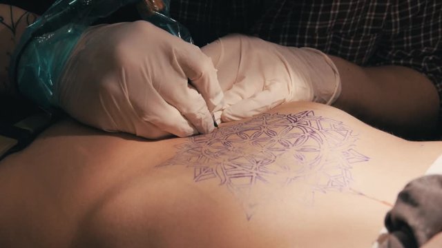 Tattoo master making a tattoo of mandala pattern. Close up shot of hands