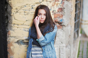 Sad lonely girl with long hair in black scarf on the background of an old crumbling brick wall, close-up