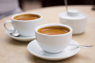 Two cups of coffee and sugar bowl on marble table