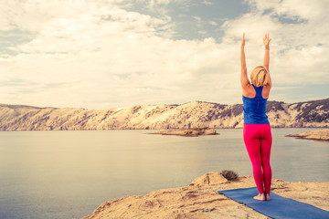 Woman meditating in yoga tree pose at the sea and mountains