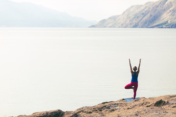 Woman meditating in yoga tree pose at the sea and mountains