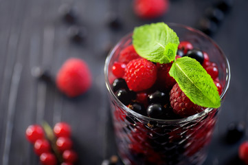 Mix of fresh berries in glass on rustic dark wooden background