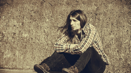 Man long haired sitting alone sad on grunge wall