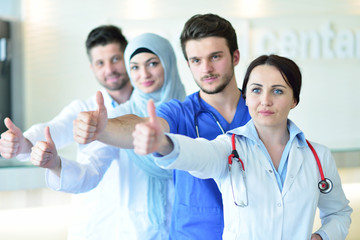 Fototapeta premium healthcare and medicine concept - attractive male doctor in front of medical group in hospital showing thumbs up