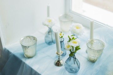 Fototapeta na wymiar Decor of photostudio - white candles, white and gray pillows, blue textile, artificials flowers