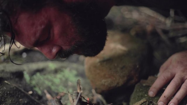 A male camper blows onto a small campfire to start it in slow motion.