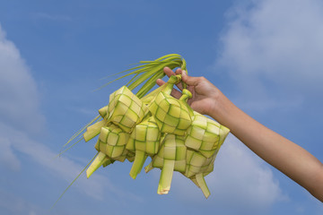 A hand holding Ketupat - Malay cuisine made from glutinous rice packed inside a diamond shaped container of wooven palm leaf.
