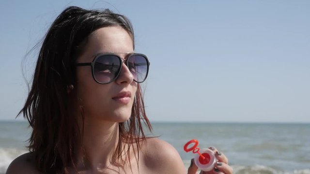 Beautiful Caucasian brunette blowing soap bubbles 4K 3840X2160 UHD video - Young female playing with air-bubbles near sea coast slow motion lifestyle 2160p 30fps UltraHD footage 