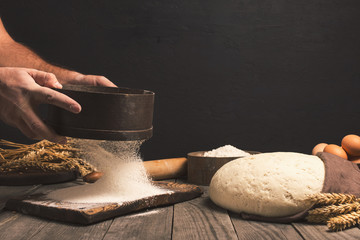 Baker sifts through the flour on a wooden table