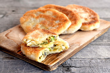 Fried pies stuffed with mushrooms, hard-boiled eggs, green onions and dill on a wooden board. Breakfast, picnic snack idea. Pies from unleavened dough