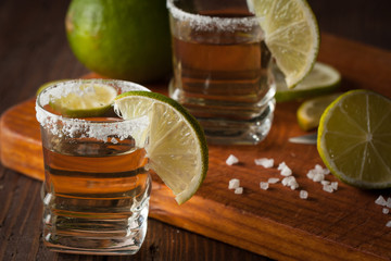 Macro photo of shots of gold Mexican tequila with lime and salt on wooden rustic background....