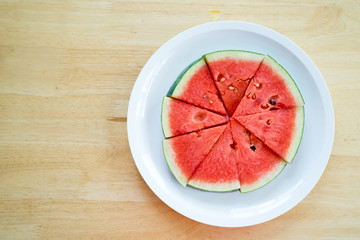 Watermelon slice on a white plate on a wood background, Top view