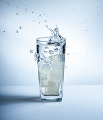 Ice cubes with water splash in glasses on blue background