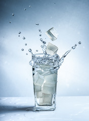 Ice cubes with water splash in glasses on blue background