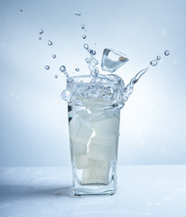 Ice cubes with water splash in glasses on blue background