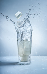 Ice cubes with water splash in glasses on blue background