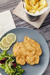 Fried chicken breast fillet on a gray plate with fries. Country style