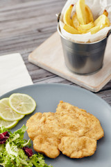 Fried chicken breast fillet on a gray plate with fries. Country style