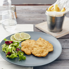 Fried chicken breast fillet on a gray plate with fries. Country style