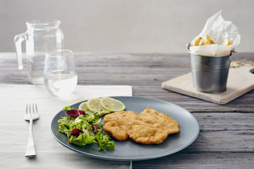 Fried chicken breast fillet on a gray plate with fries. Country style