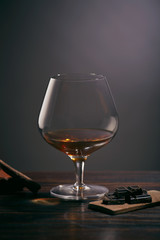 Glass of brandy on a wooden table with chocolate and cigar. gray background.