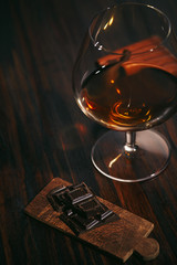 Glass of brandy on a wooden table with chocolate and cigar. gray background.