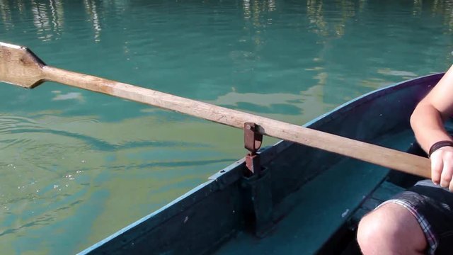 Person paddling blue boat with oar in beautifull lake with blue water. Close-up