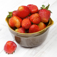 Fresh organic strawberries in bowl on white wooden background