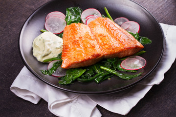 Broiled salmon with radish and spinach, served on black plate. View from above, top studio shot