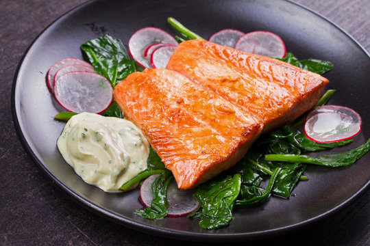 Broiled salmon with radish and spinach, served on black plate. View from above, top studio shot