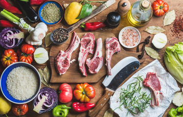 Ingredients for cooking dinner. Raw uncooked lamb meat chops, rice, oil, spices and vegetables over wooden background, top view