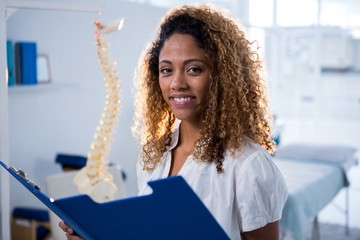 Smiling physiotherapist holding clipboard in clinic - Powered by Adobe