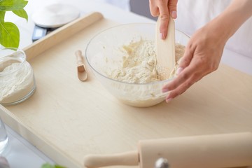 Woman mixing pizza dough with wooden spatula.