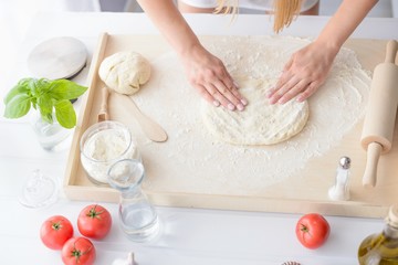 Woman kneading pizza dough on wooden pastry board.