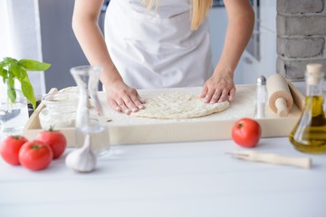 Woman kneading pizza dough on wooden pastry board.