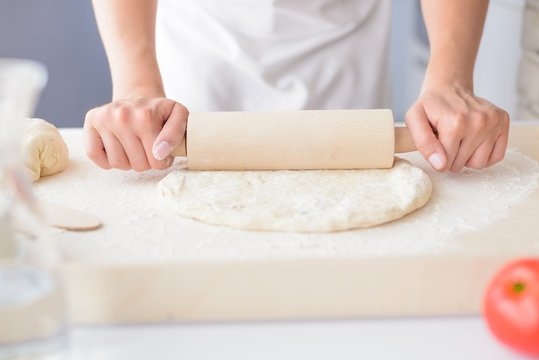 Woman rolling pizza dough using rolling pin.
