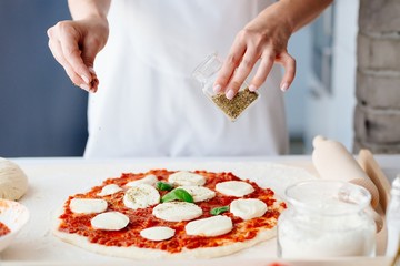 Obraz na płótnie Canvas Woman adding oregano on raw pizza.