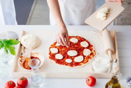 Woman puts slices of mozzarella on the pizza