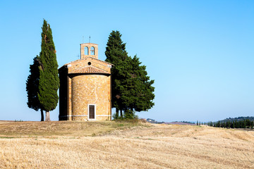 une chapelle toscane isolée sur le haut d'un champs de blé