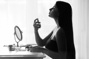 Beautiful young woman looking in mirror while using perfume. Black and white
