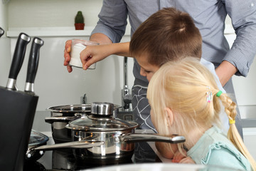 Small boy with girl salting food with  father in the kitchen