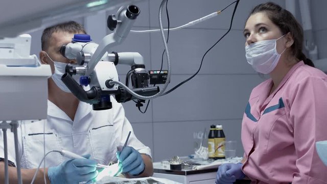 Male dentist receiving the root canals of the patient using the microscope.
