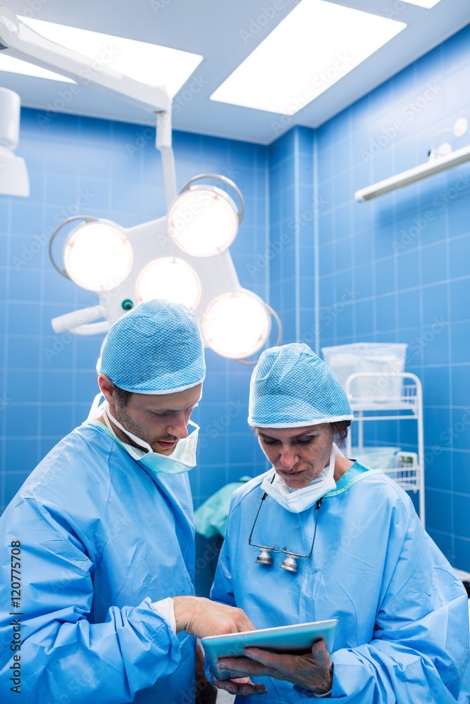 Poster surgeons discussing over digital tablet in operation room