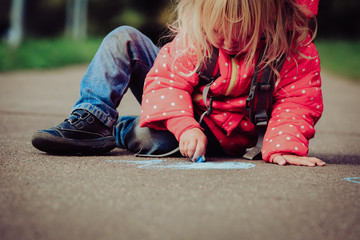 little girl drawing with chalks on asphalt after school