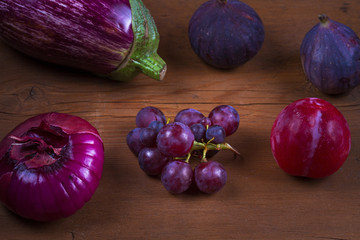 Ripe purple figs, plums, grape, eggplant and onion. Fruit and vegetable still life on wooden background. Clean eating concept. Colorful food collage