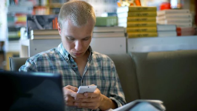 Student sitting on the couch in the library and texting on smartphone
