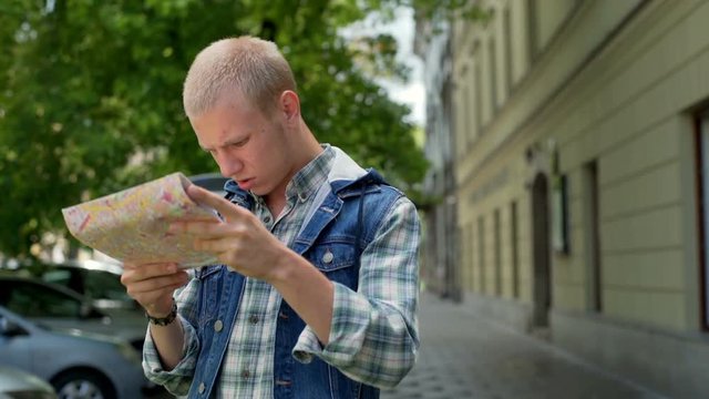 Boy looking lost while standing on pathway and reading map
