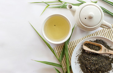 teapot and cup of herbal green tea on bamboo with white table background. over light