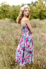 Young girl in flower wreath walking in meadow