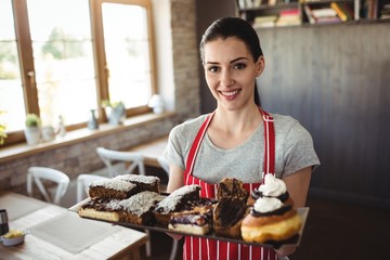 Portrait of female baker holding a tray of sweet foods